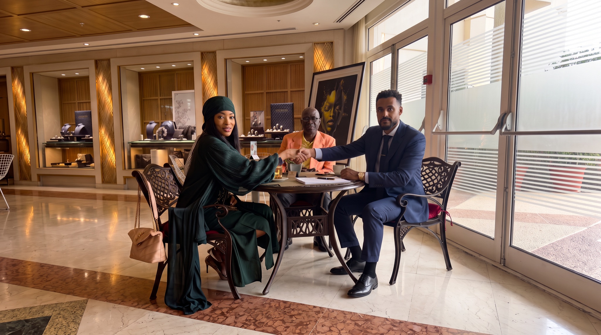 Three people at a table in a hotel lobby in Geneva; two of them shake hands over signed papers.